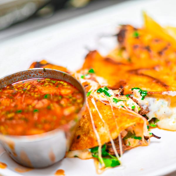 Close-up of crispy Los 3 Regios birria tacos with melted cheese and a side of consome.