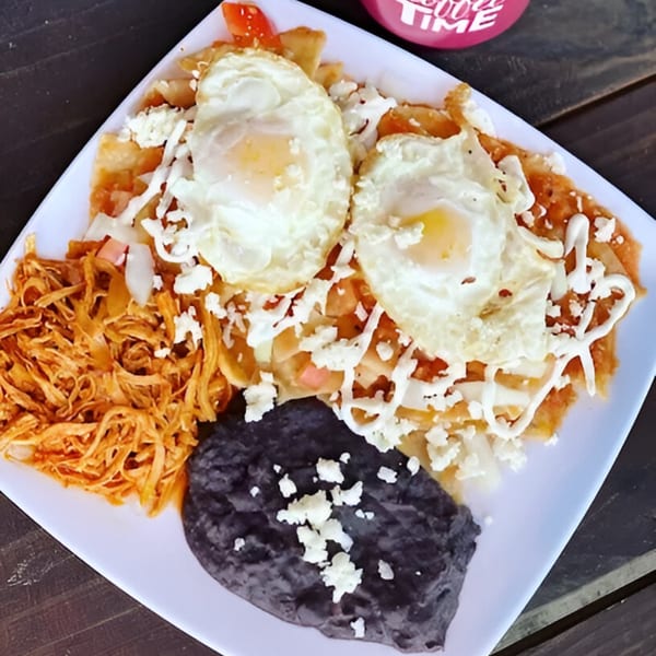 Chilaquiles with two fried eggs, shredded chicken, and black beans on a white plate.