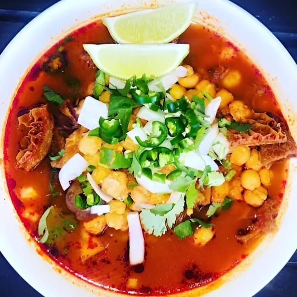 Close-up of a bowl of Los 3 Regios Mexican Restaurant's menudo soup, garnished with lime, cilantro, and jalapeños.
