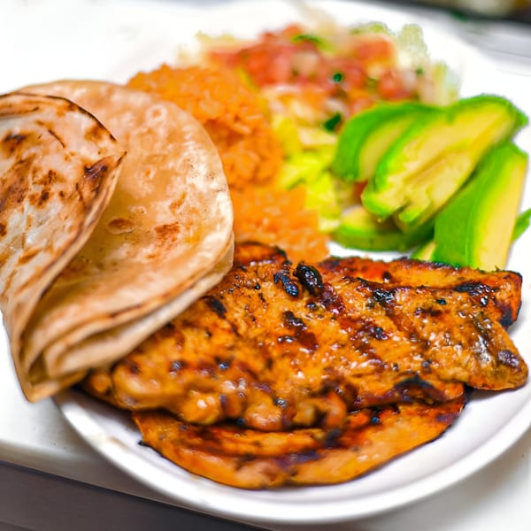 Grilled chicken with tortillas, rice, avocado slices, and pico de gallo on a white plate.