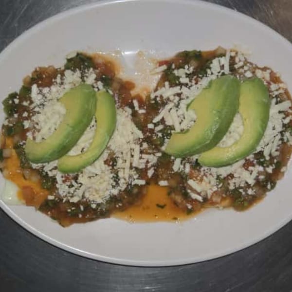 Two Mexican dishes with salsa, shredded cheese, and avocado slices on a white plate.