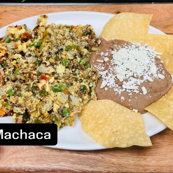 Machaca with scrambled eggs, vegetables, refried beans topped with cheese, and tortilla chips.
